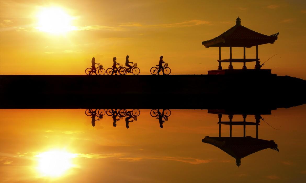 Reflection of cyclists riding on a concrete barrier in Sanur beach at sunrise